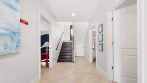 A hallway with a staircase, a red chair, and a door. - The Hammock Dunes Collection (Orange Beach)