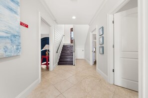 A hallway with a staircase, a red chair, and a door. - The Hammock Dunes Collection (Orange Beach)