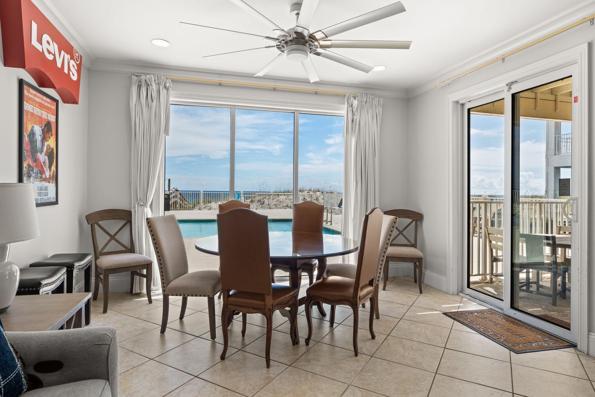 A dining area with a view of the beach, a ceiling fan, and a Levi's sign.