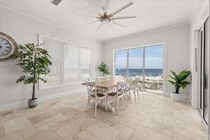 Une pièce spacieuse avec une grande table et des chaises, un ventilateur de plafond et une vue sur la plage.
