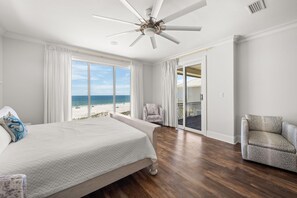 Une chambre avec un grand lit, une chaise, un ventilateur de plafond et une vue sur la plage.