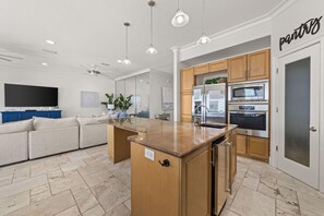 A modern kitchen with a central island, wooden cabinets, stainless steel appliances, and a built-in oven. - The Hammock Dunes Collection (Orange Beach)