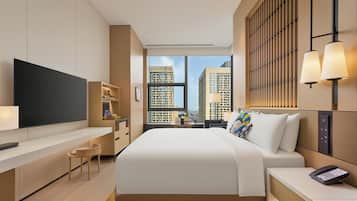 Habitación de hotel moderna con una cama grande, un televisor de pantalla plana, un escritorio y vistas a edificios altos.