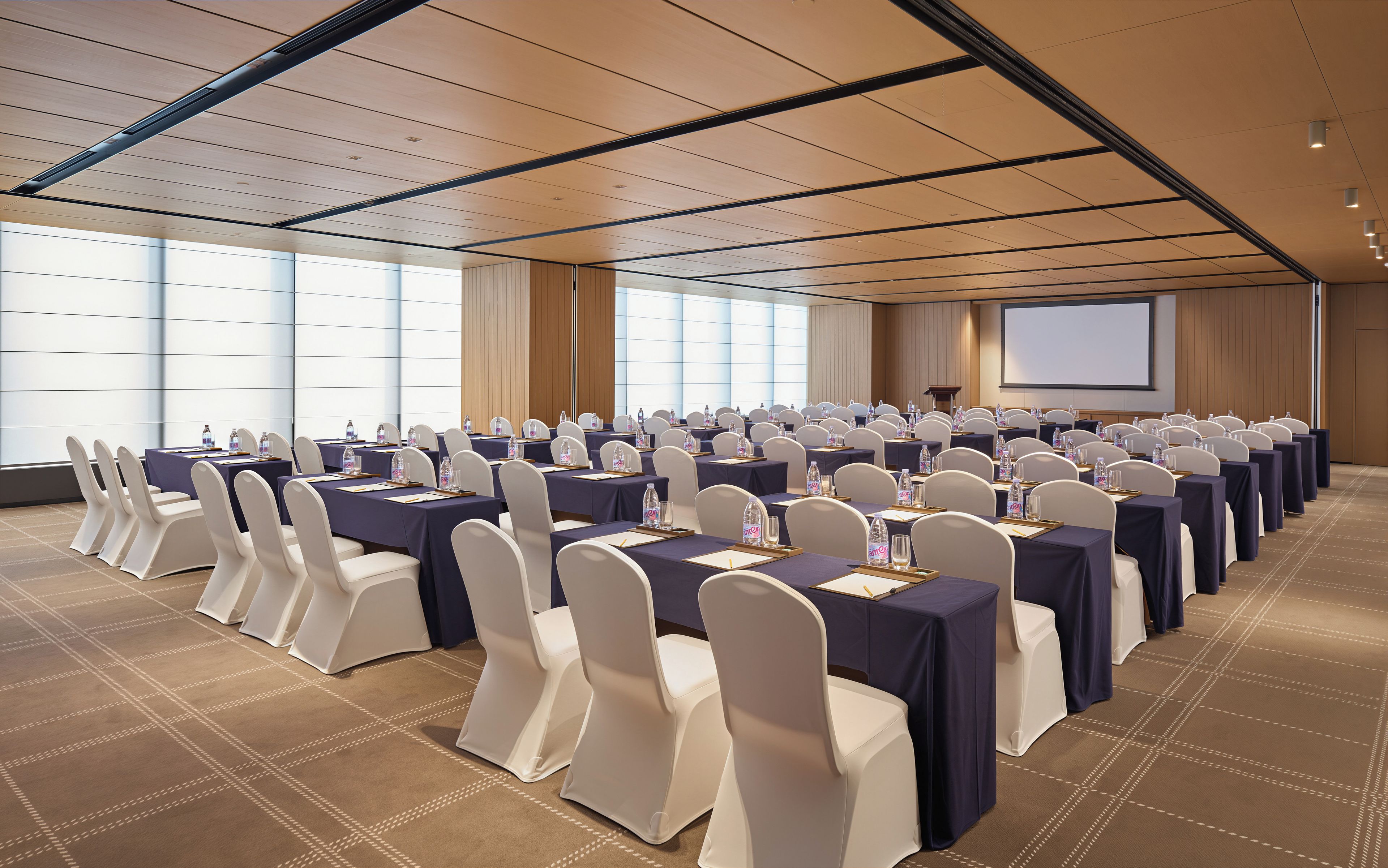 A conference room with rows of tables and chairs, a projector screen, and a podium.