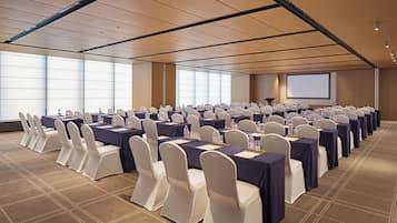 A conference room with rows of tables and chairs, a projector screen, and a podium.