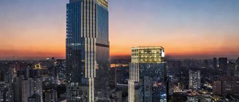 A cityscape with two prominent skyscrapers, one taller than the other, surrounded by other buildings and a sunset sky.