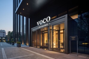 A modern hotel entrance with a glass facade, a prominent 'VOCO' sign, and a well-lit interior visible through the doors. - Voco Shenyang Golden Corridor By Ihg (Shenyang)