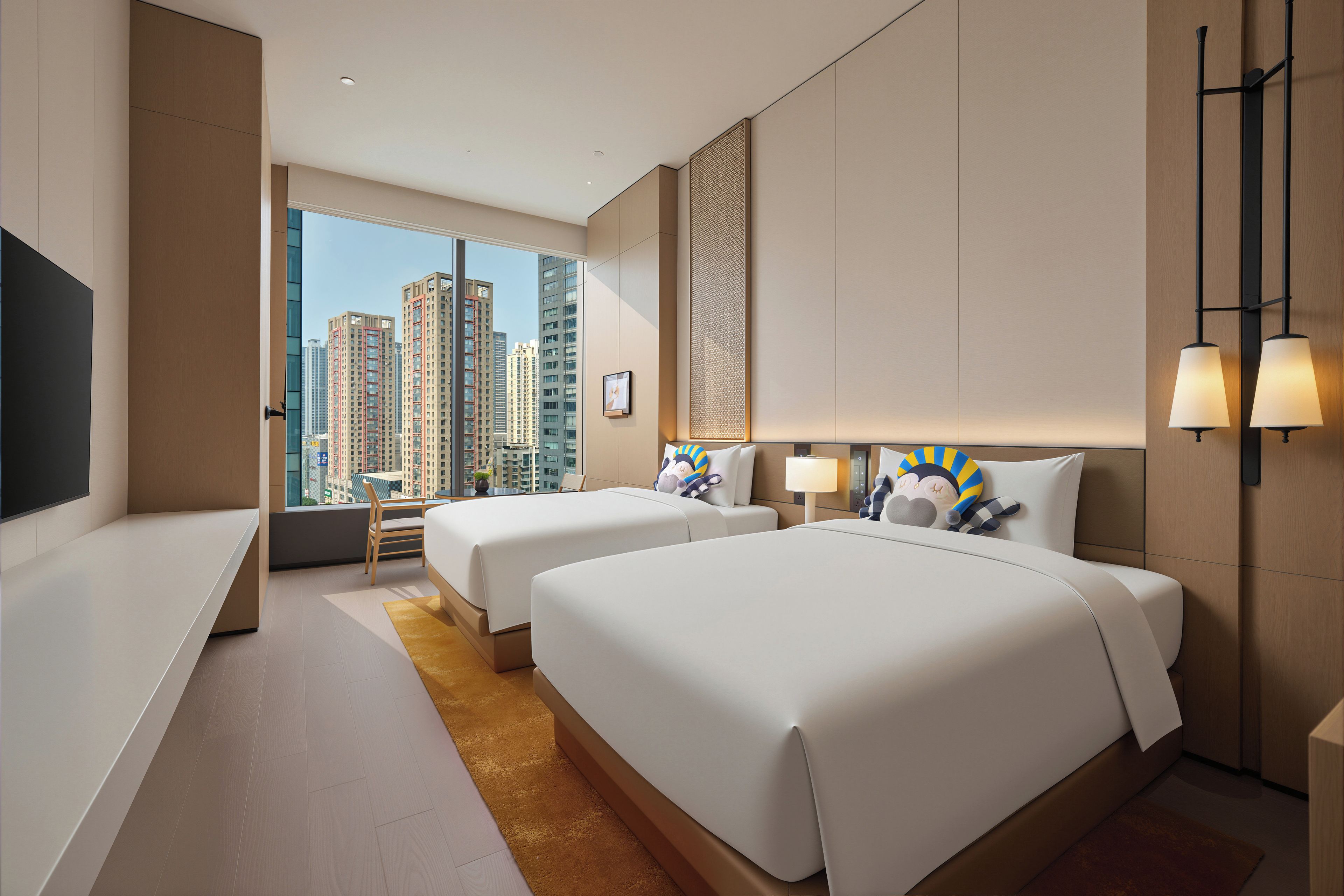 A hotel room with two beds, a desk, and a large window offering a city view.