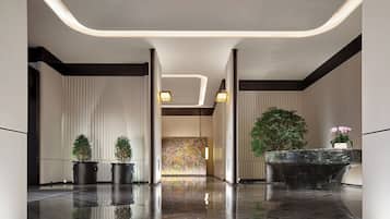 Un lobby moderno con piso reflectante, persianas verticales y una recepción con planta.