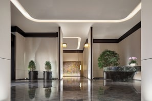 A modern lobby with a reflective floor, vertical blinds, and a reception desk with a plant.