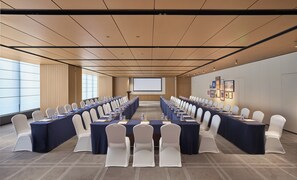 Una sala conferenze con un lungo tavolo, sedie bianche e uno schermo per proiezioni.