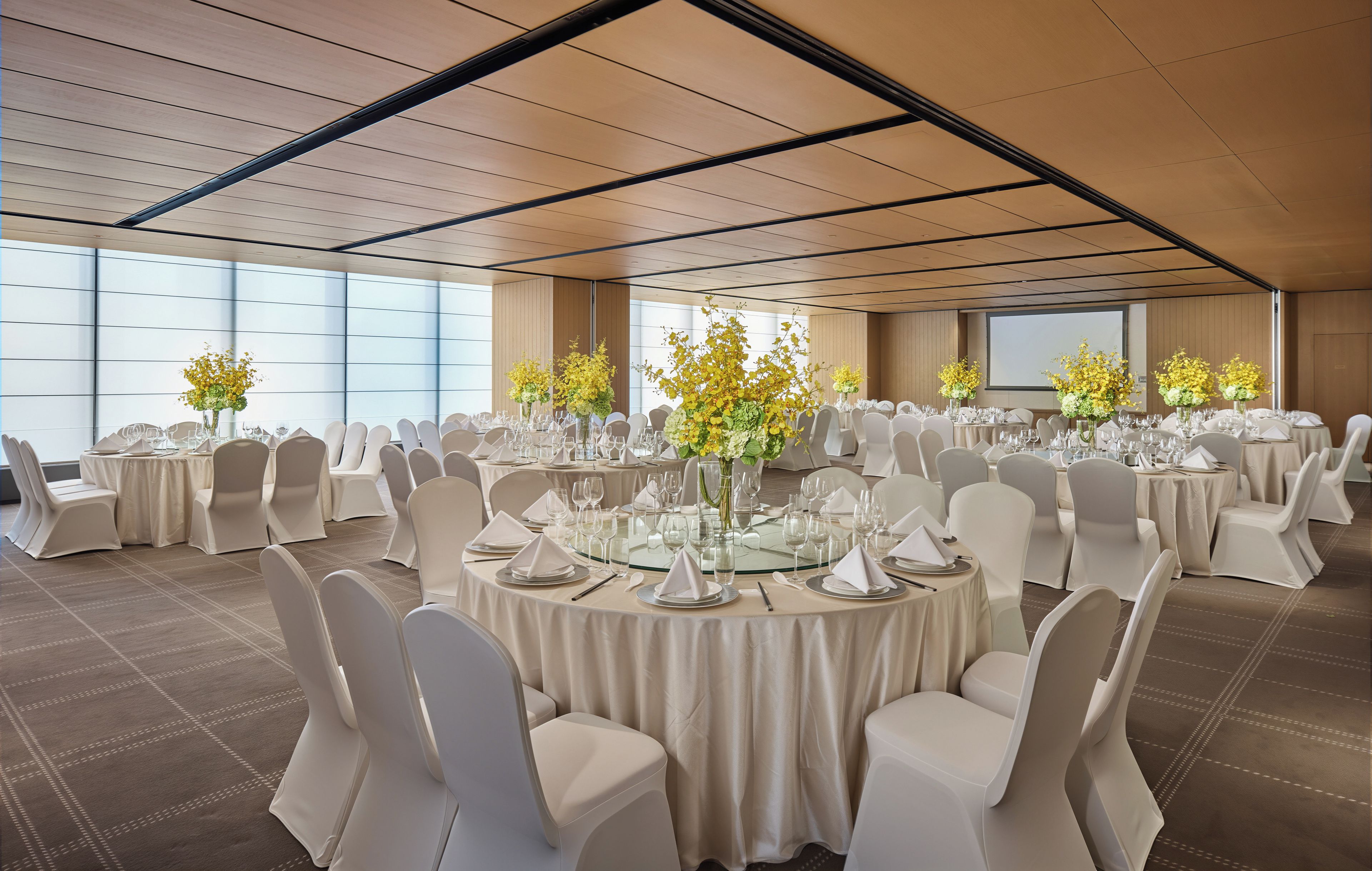 A conference room with round tables, white chairs, and floral centerpieces.