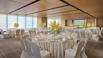 A conference room with round tables, white chairs, and floral centerpieces.