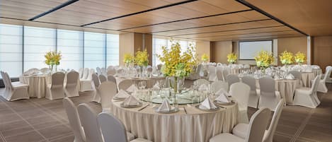 A conference room with round tables, white chairs, and floral centerpieces.