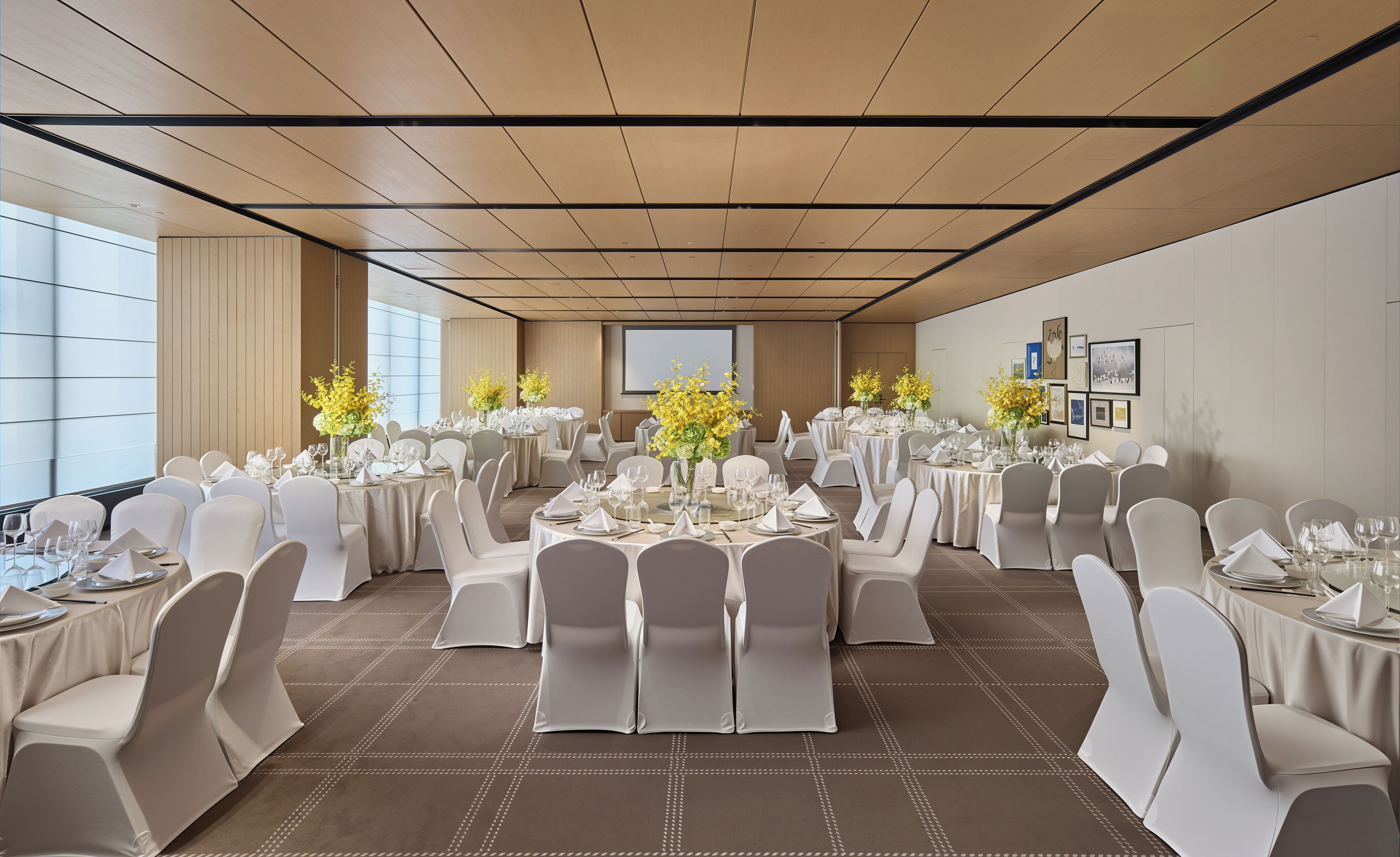 Un salón de banquetes con mesas redondas, sillas blancas y centros de mesa florales.