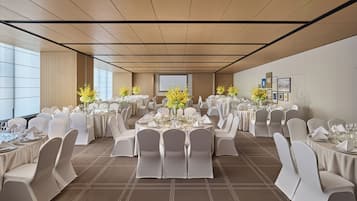 Un salón de banquetes con mesas redondas, sillas blancas y centros de mesa florales.