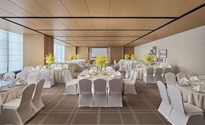 A banquet hall with round tables, white chairs, and floral centerpieces.