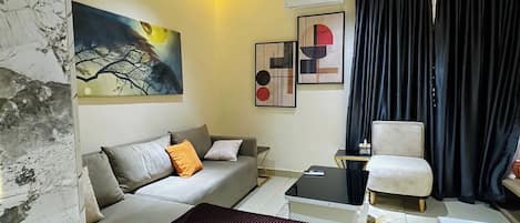 A modern bedroom with a bed, sofa, armchair, and a painting on the wall.
