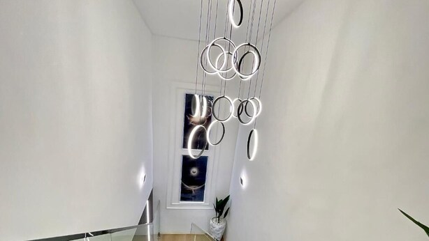 Un interior moderno con una escalera, barandilla de cristal y una lámpara colgante.