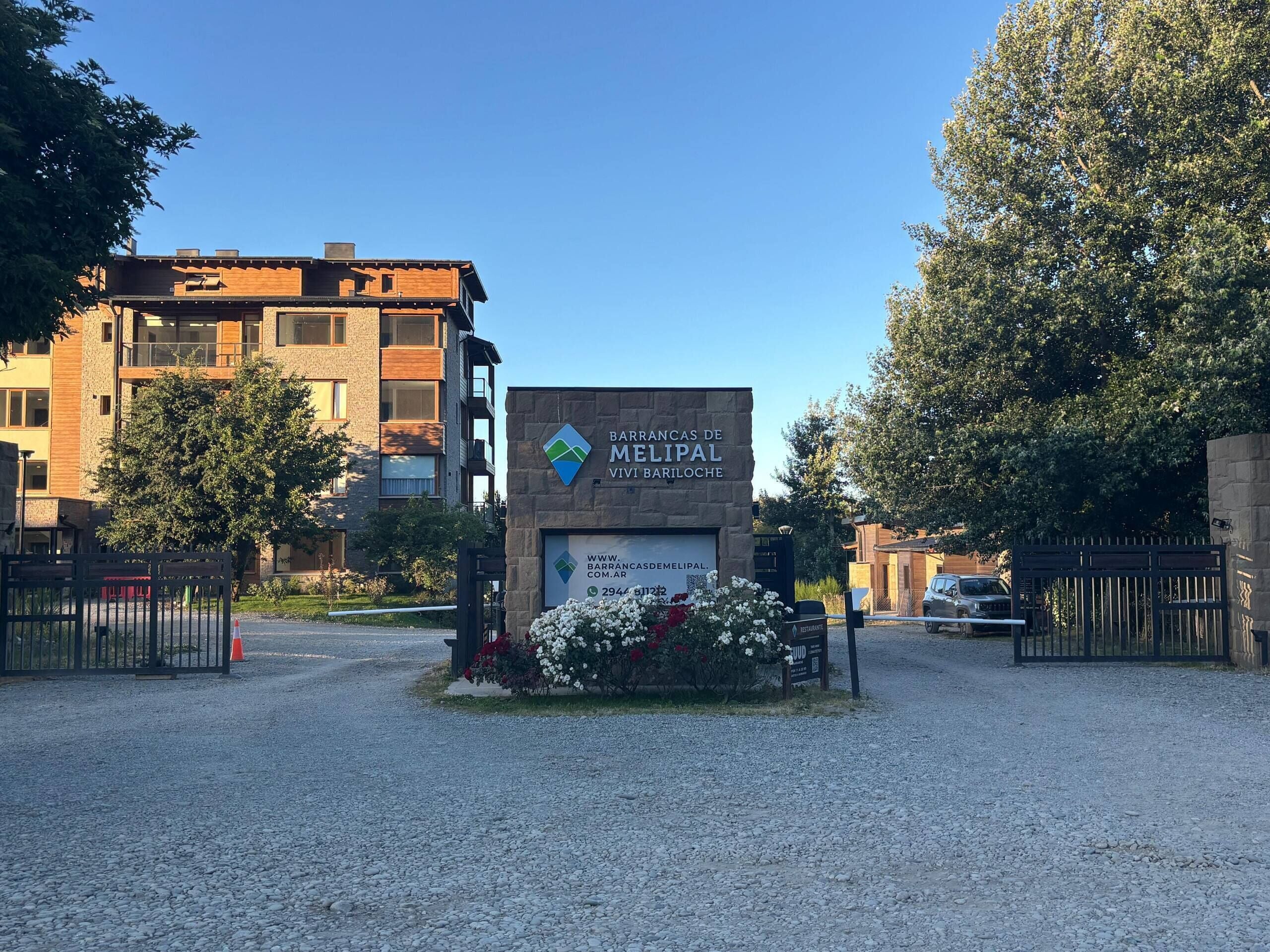 A gated entrance to a residential building with a sign indicating 'Barrancas de Melipal Vivi Bariloche.'