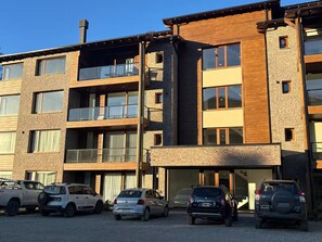 Um edifício residencial de vários andares com entrada para garagem, carros estacionados e céu claro.