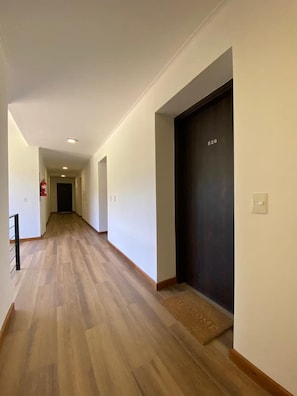 A hallway with wooden flooring, white walls, and a dark-colored elevator door. - Lake, Mountains, and Comfort · Cozy and Bright Apartment (San Carlos de Bariloche)