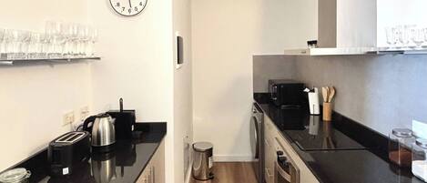A modern kitchen with black countertops, stainless steel appliances, and wooden flooring.