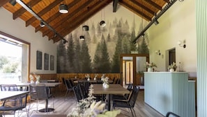 A restaurant with a high wooden ceiling, hanging pendant lights, and a mural of trees on the wall. - Lake, Mountains, and Comfort · Bright and Cozy Apartment (San Carlos de Bariloche)