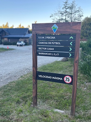 A directional sign with arrows pointing to various facilities such as a swimming pool, soccer field, sector houses, and barrancas. - Lake, Mountains, and Comfort · Cozy and Bright Apartment (San Carlos de Bariloche)