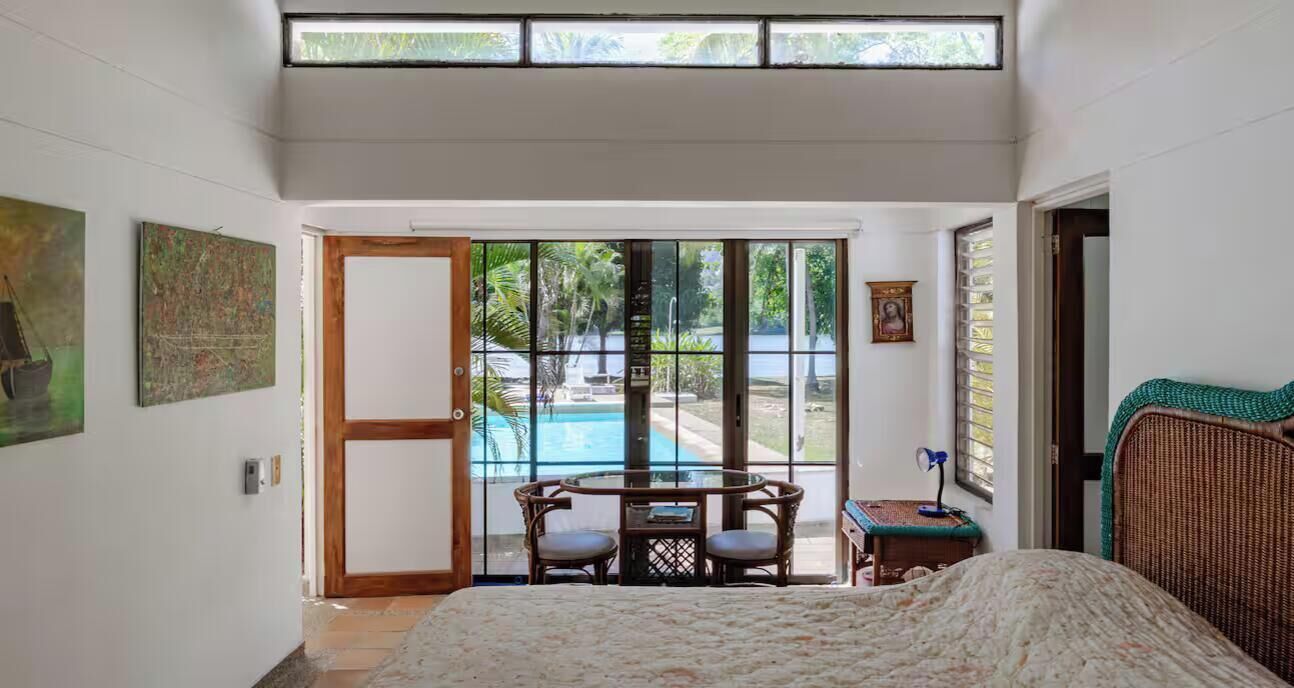Un dormitorio con cama, ventana, puerta que da a un balcón y vista a una piscina.