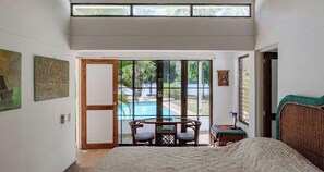 Ein Schlafzimmer mit einem Bett, einem Fenster, einer Tür, die auf einen Balkon führt, und Blick auf einen Pool.