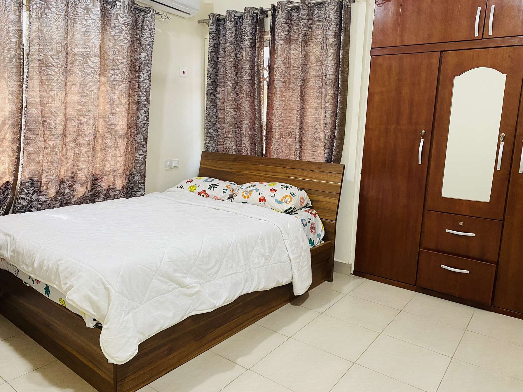 Une chambre à coucher avec un lit en bois, des rideaux à motifs et une armoire avec un miroir.
