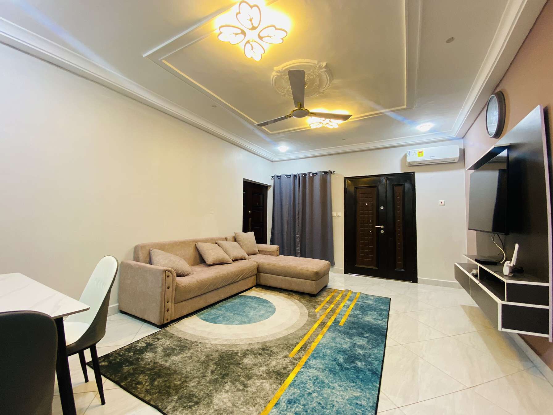 A living room with a sectional sofa, a dining table with chairs, a flat-screen TV, and a ceiling fan.