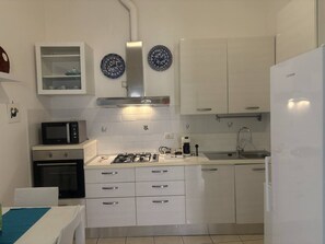 A compact kitchen with white cabinetry, a microwave, a stove, and a sink. - Casa Mare Teulada (Teulada)