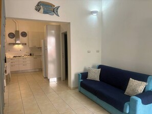A living room with a sofa and a kitchen in the background. - Casa Mare Teulada (Teulada)