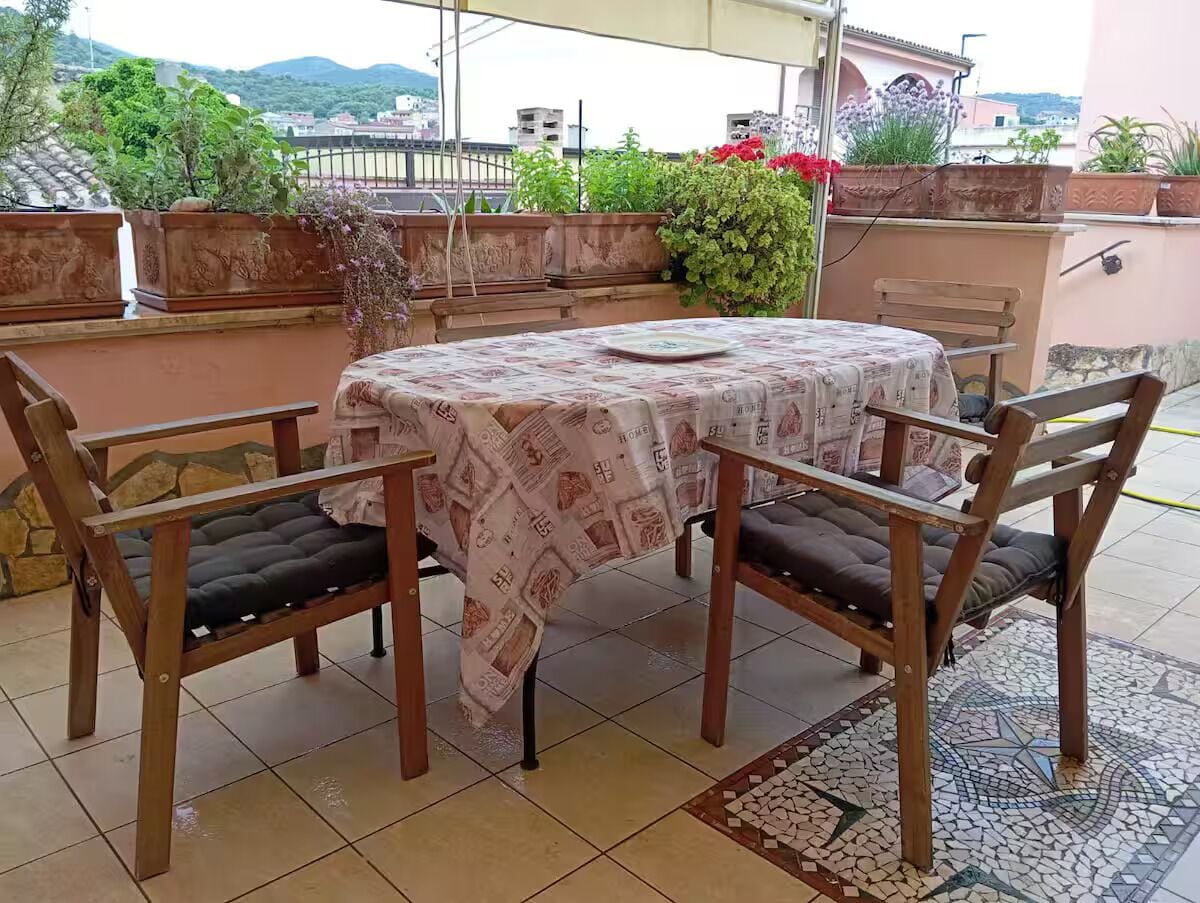 A round table with a patterned tablecloth, two wooden chairs with cushions, and a tiled floor with a decorative border.