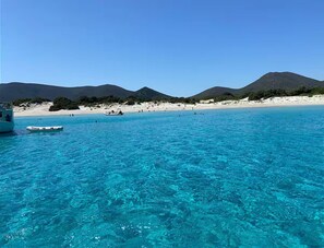 A clear blue sea with a boat and a sandy beach, surrounded by hills. - Casa Mare Teulada (Teulada)