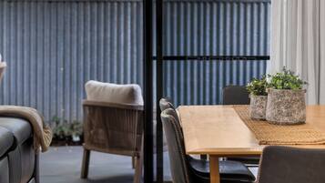 A modern dining area with a wooden table and chairs, a grey sofa, and a view of greenery through a glass door.