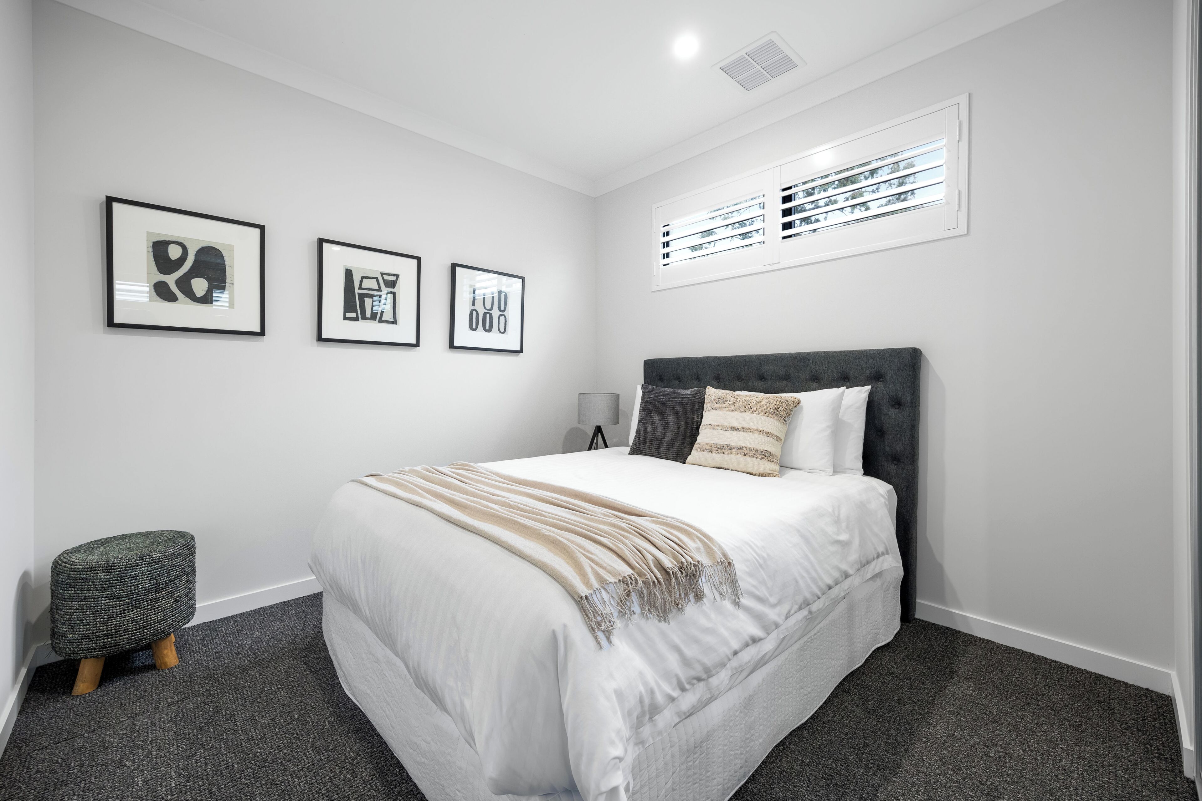A bedroom with a bed, a bedside table, a lamp, and three framed artworks on the wall.