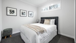 A bedroom with a bed, a bedside table, a lamp, and three framed artworks on the wall. - The Torrens A Contemporary Escape in the Foothills (Kingswood)