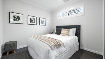 A bedroom with a bed, a bedside table, a lamp, and three framed artworks on the wall.