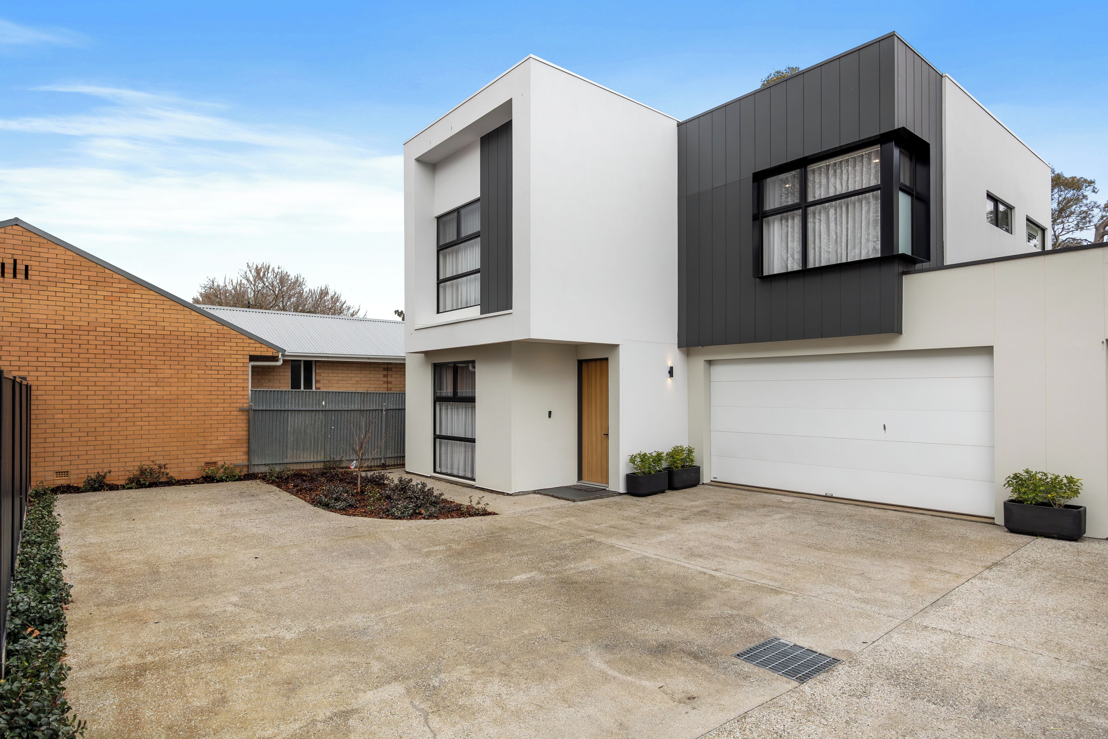 A modern two-story house with a garage, a brick wall, and a small garden area.