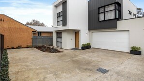 A modern two-story house with a garage, a brick wall, and a small garden area. - The Torrens A Contemporary Escape in the Foothills (Kingswood)