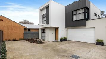 A modern two-story house with a garage, a brick wall, and a small garden area.