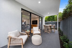 Eine moderne Außenveranda mit Sitzgelegenheiten, einem Fernseher und Blick ins Innere.