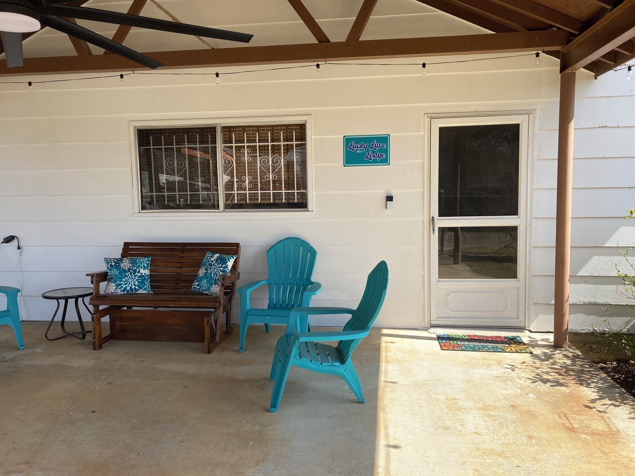 A covered patio area with a wooden bench, two turquoise chairs, and a small table.
