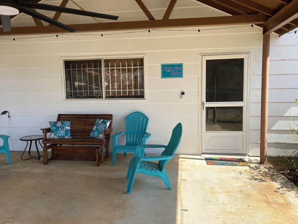 A covered patio area with a wooden bench, two turquoise chairs, and a small table.