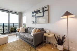 Ein modernes Wohnzimmer mit einem grauen Sofa, einem runden Beistelltisch, einer Stehlampe und einem großen abstrakten Gemälde an der Wand.