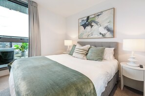 Ein Hotelzimmer mit einem Bett, zwei Nachttischen, einem Vorhangfenster und einem Bild an der Wand.