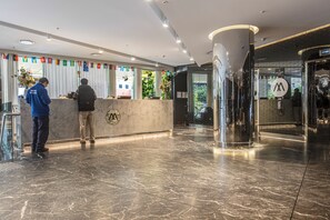 Ein Hotel-Empfangsbereich mit Marmorboden, einer Rezeption und einem Glastauschlift.